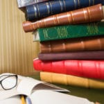 girl in graduation cap looking at high heap of books on table at