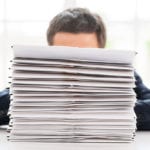 So much work to do! Businessman hiding behind a stack of documents laying on the table