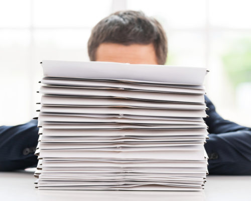 So much work to do! Businessman hiding behind a stack of documents laying on the table